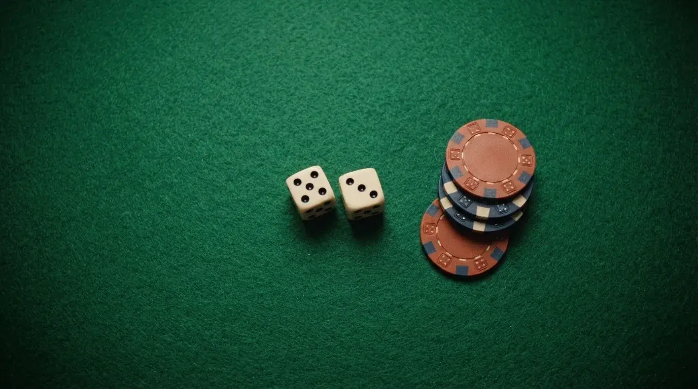 Vista cenital de fichas de casino y dados sobre una mesa de fieltro verde bajo luz suave.